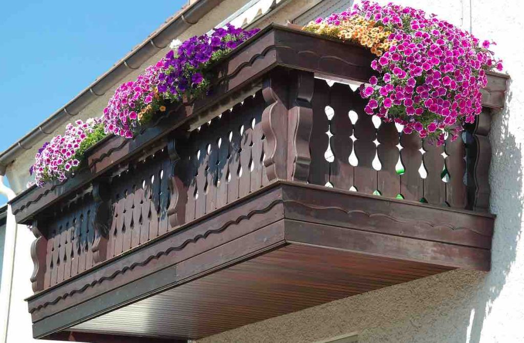 En brunbeiset balkong med masse blomster på et hvitt hus